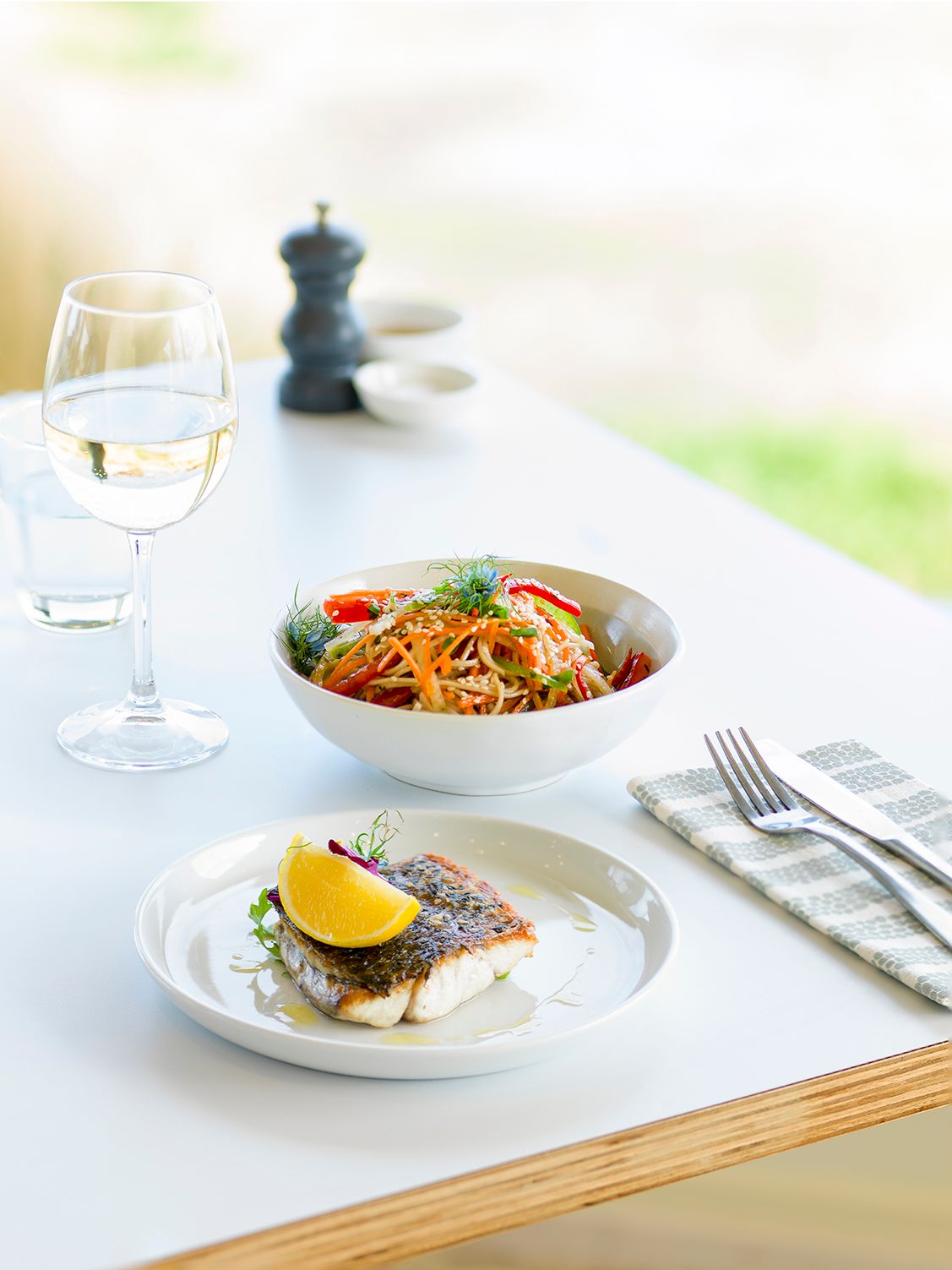 Pan-fried fish fillet with lemon and Asian noodle salad, professionally styled on a restaurant table