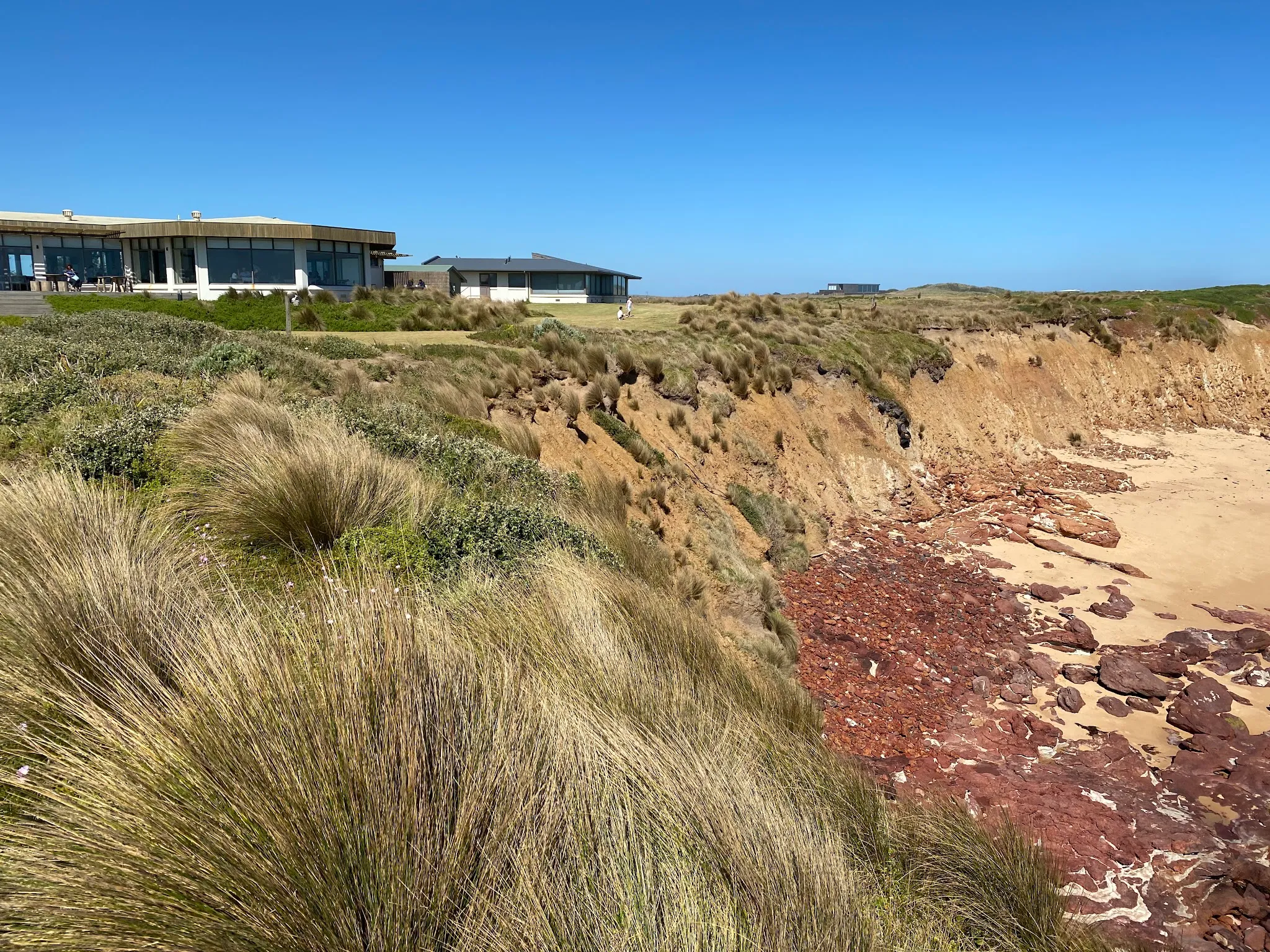 The Cape Kitchen building viewed from the beach, perched above rocky coastal cliffs on Phillip Island