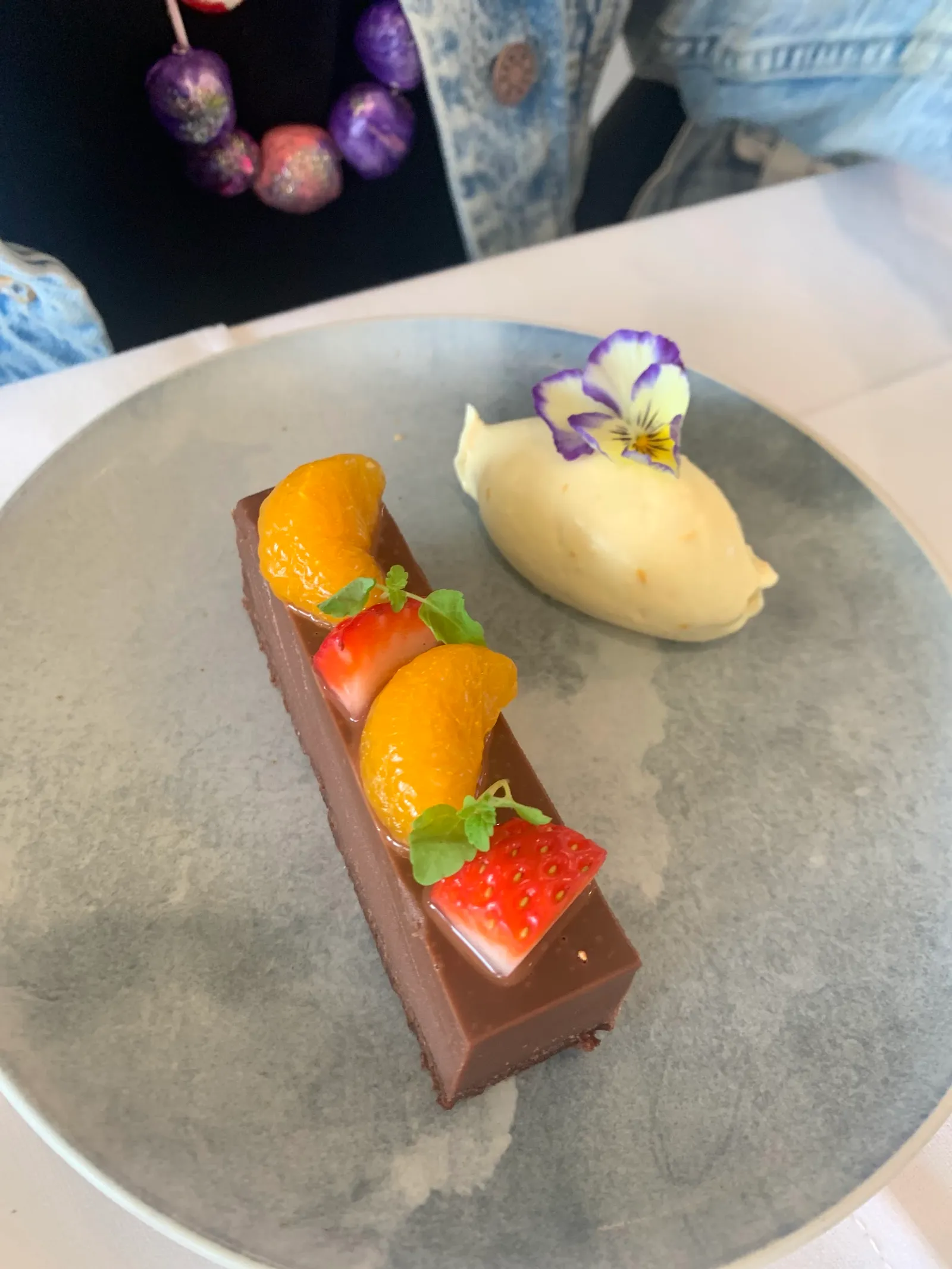 Refined chocolate tart with mandarin, strawberry and pansy flower on grey plate at The Cape Kitchen