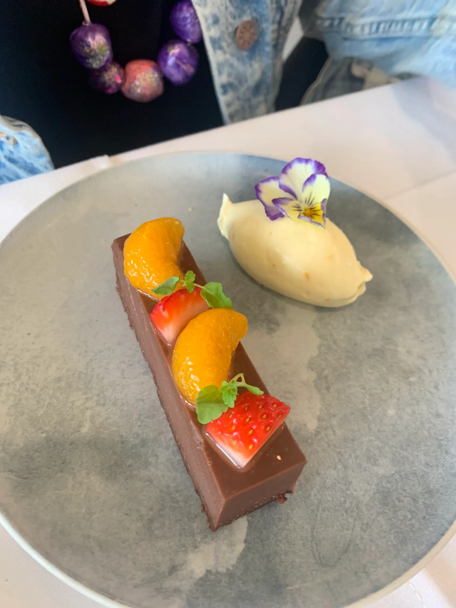 Refined chocolate tart with mandarin, strawberry and pansy flower on a grey ceramic plate