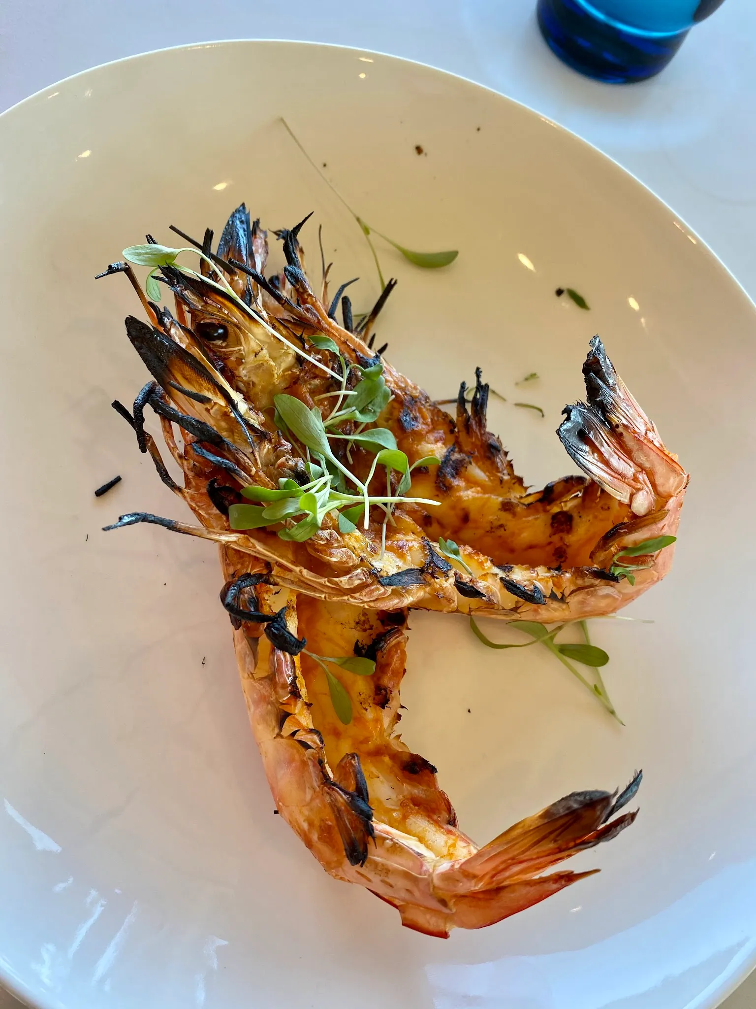 Two whole grilled king prawns with micro herbs on a white plate