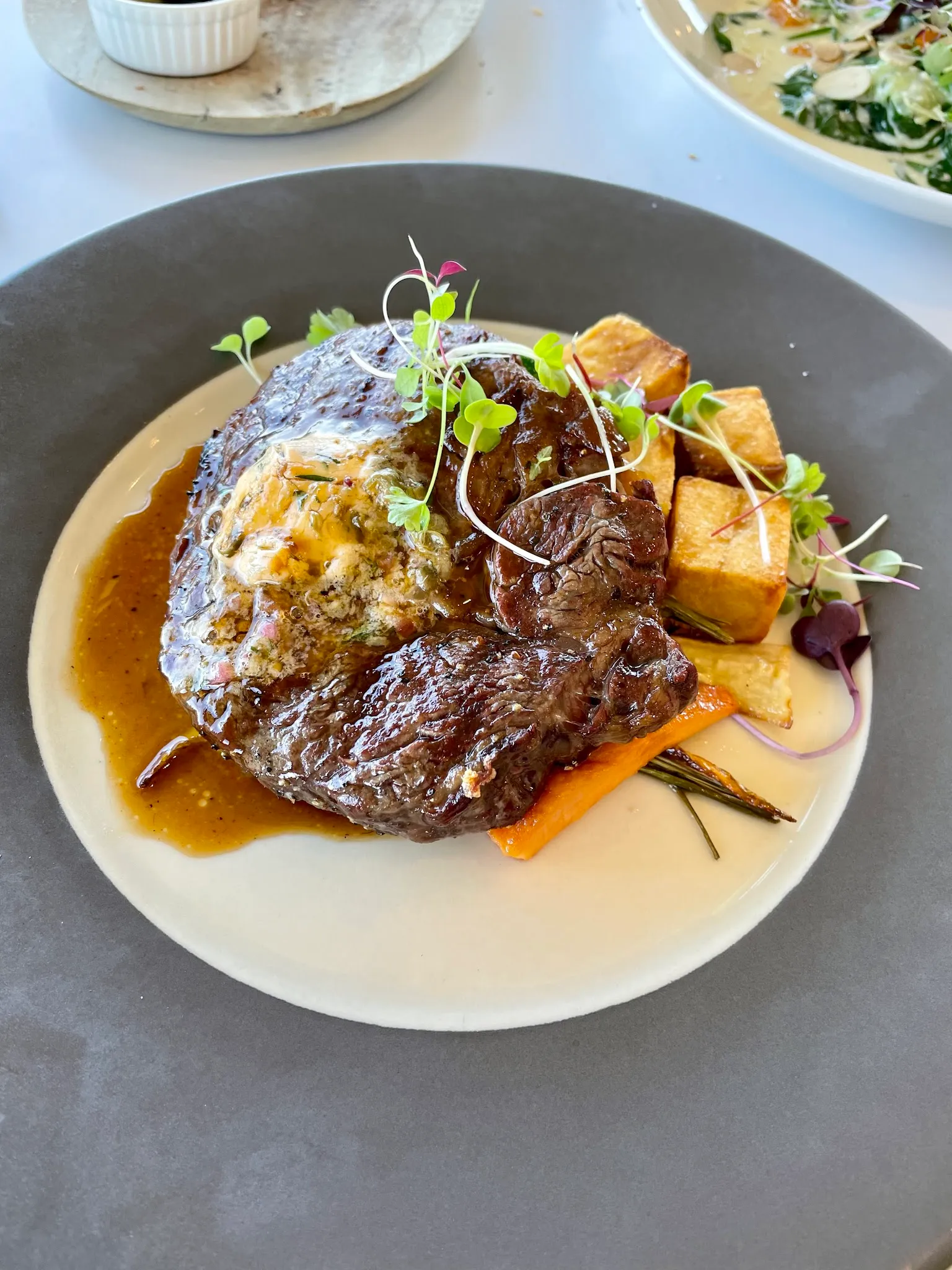 Phillip Island Scotch fillet steak with rich jus, polenta and roasted carrot on a dark grey plate