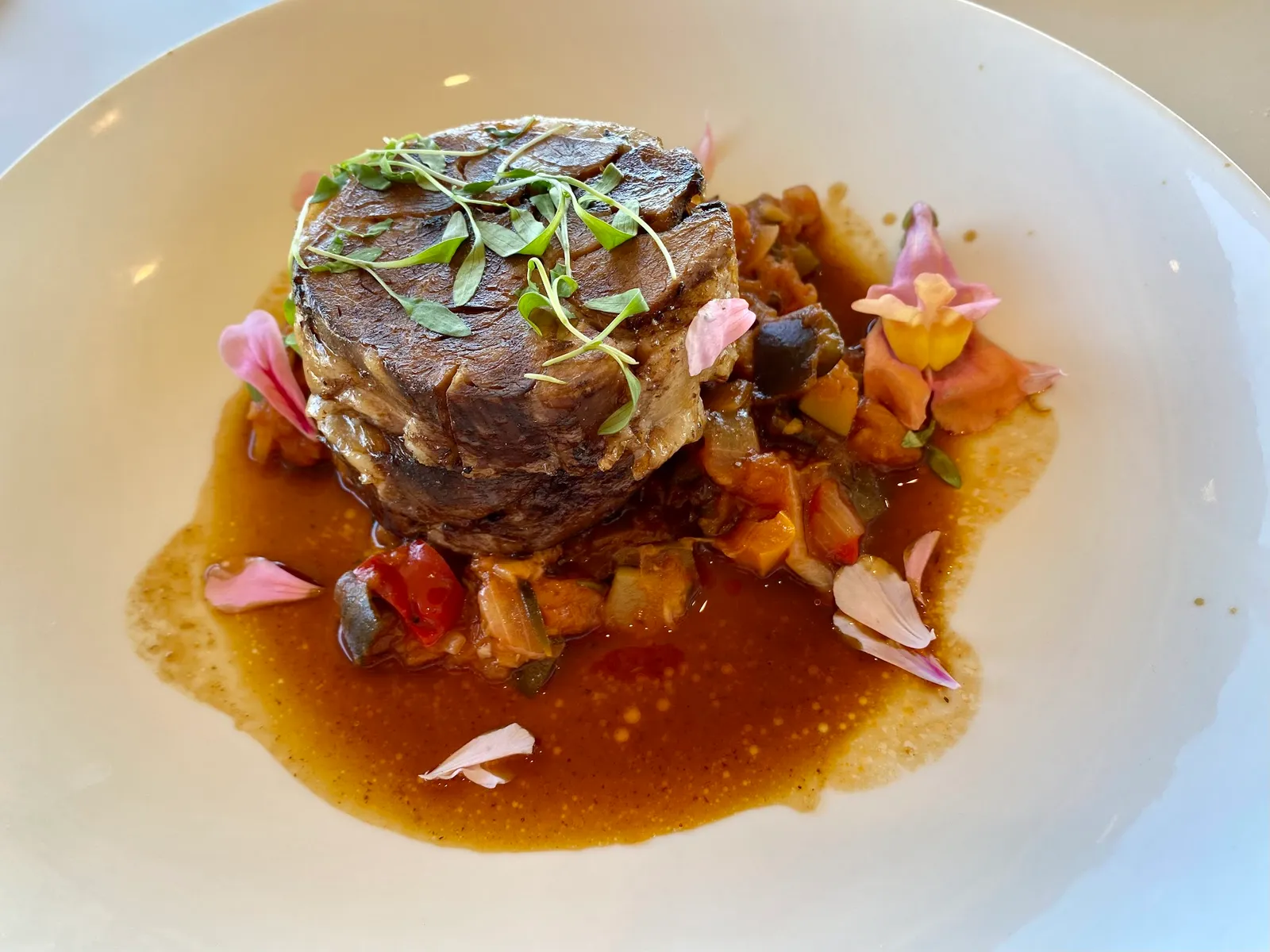 Braised beef cheek with ratatouille, edible flowers and rich jus on a white plate